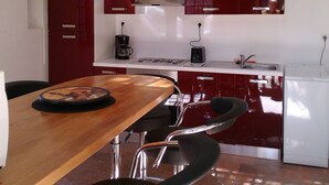A modern kitchen with red cabinets, a wooden dining table, and a white refrigerator. - the cottages of castera NORMANDIE (Aire-Sur-L'adour)