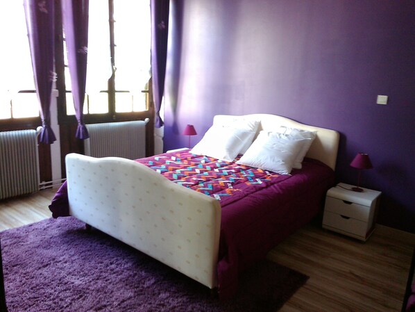 A bedroom with a bed, a nightstand, a lamp, and a window with curtains.