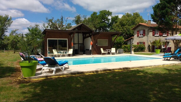 A poolside area with lounge chairs, a small table, and a covered seating area. - the cottages of castera NORMANDIE (Aire-Sur-L'adour)