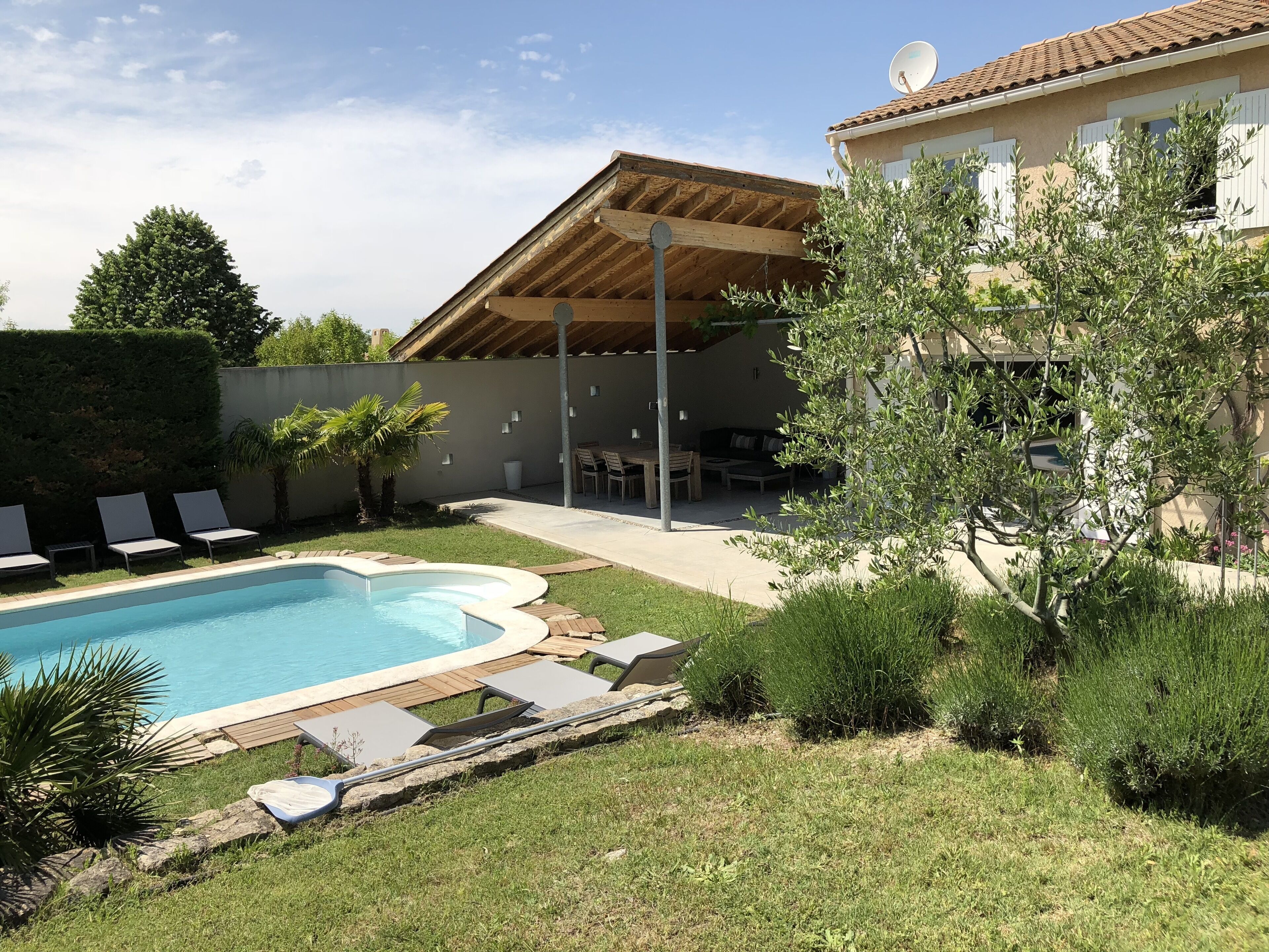 En have med swimmingpool, liggestole, en patio og en bygning med tegltag.