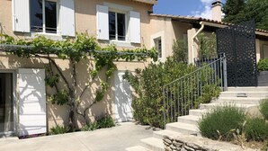 Une maison avec un escalier en pierre menant à l’entrée, une porte blanche et un jardin agrémenté de plantes et de fleurs.