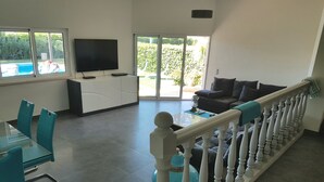 Ein geräumiger Wohnbereich mit Balkon, einem Flachbildfernseher, einem Esstisch mit Stühlen und einer Couch.