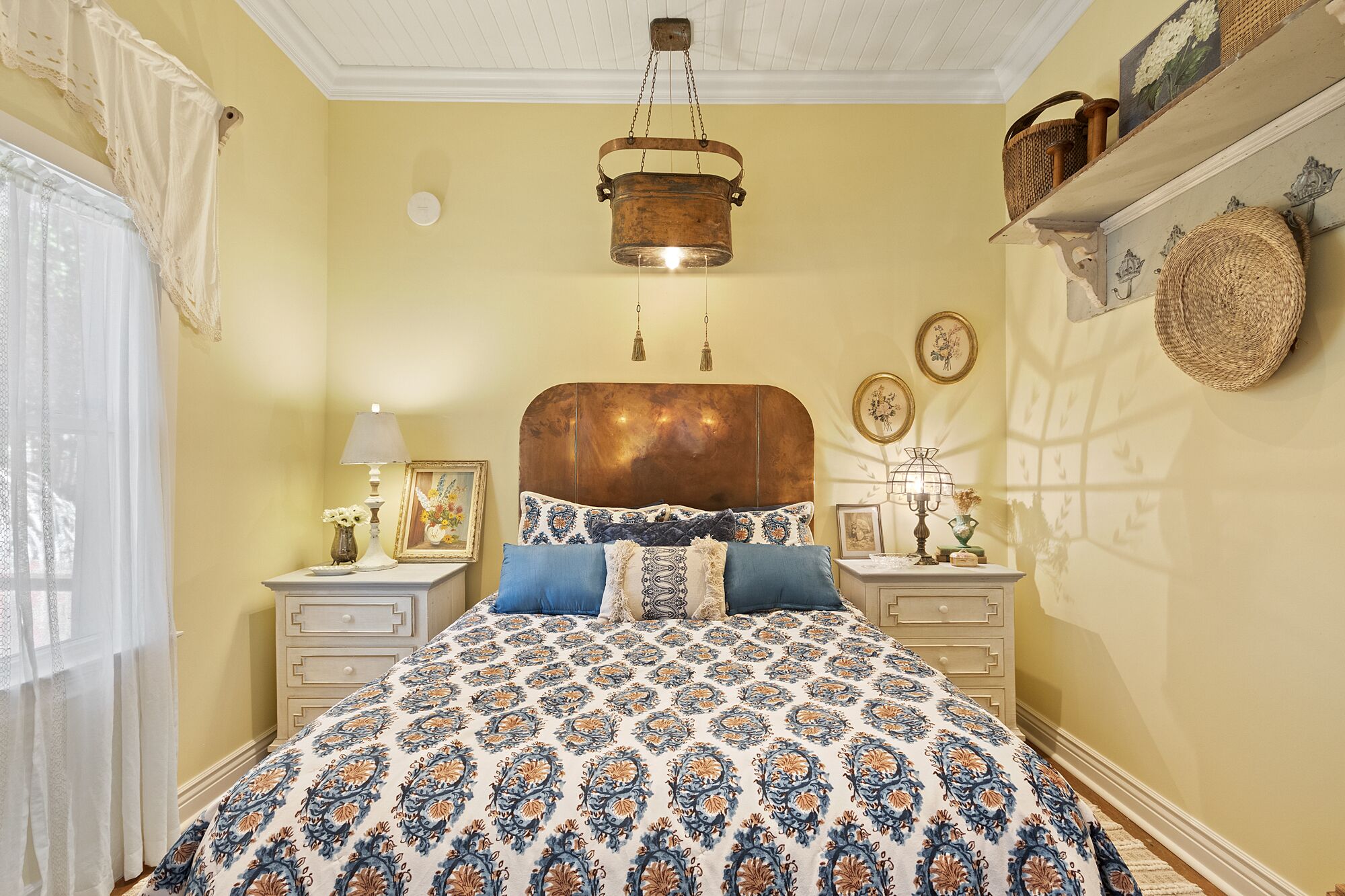 A bedroom with a patterned bedspread, a wooden headboard, bedside tables with lamps, and wall decor.