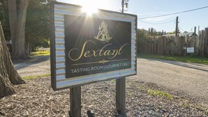 Opastekyltti, jossa lukee: ”Sextant Tasting Room | Gourmet Deli”, ja sen yläpuolella on koristeellinen riippuvalaisin.