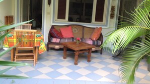 Un espace patio accueillant avec un sol à carreaux, une table en bois, un canapé en osier agrémenté de coussins colorés et un fauteuil.