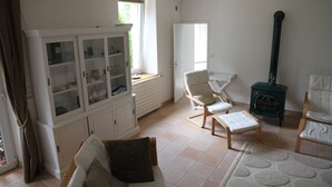Un soggiorno con un mobile bianco, due sedie di legno, un tavolino e un fornello verde.