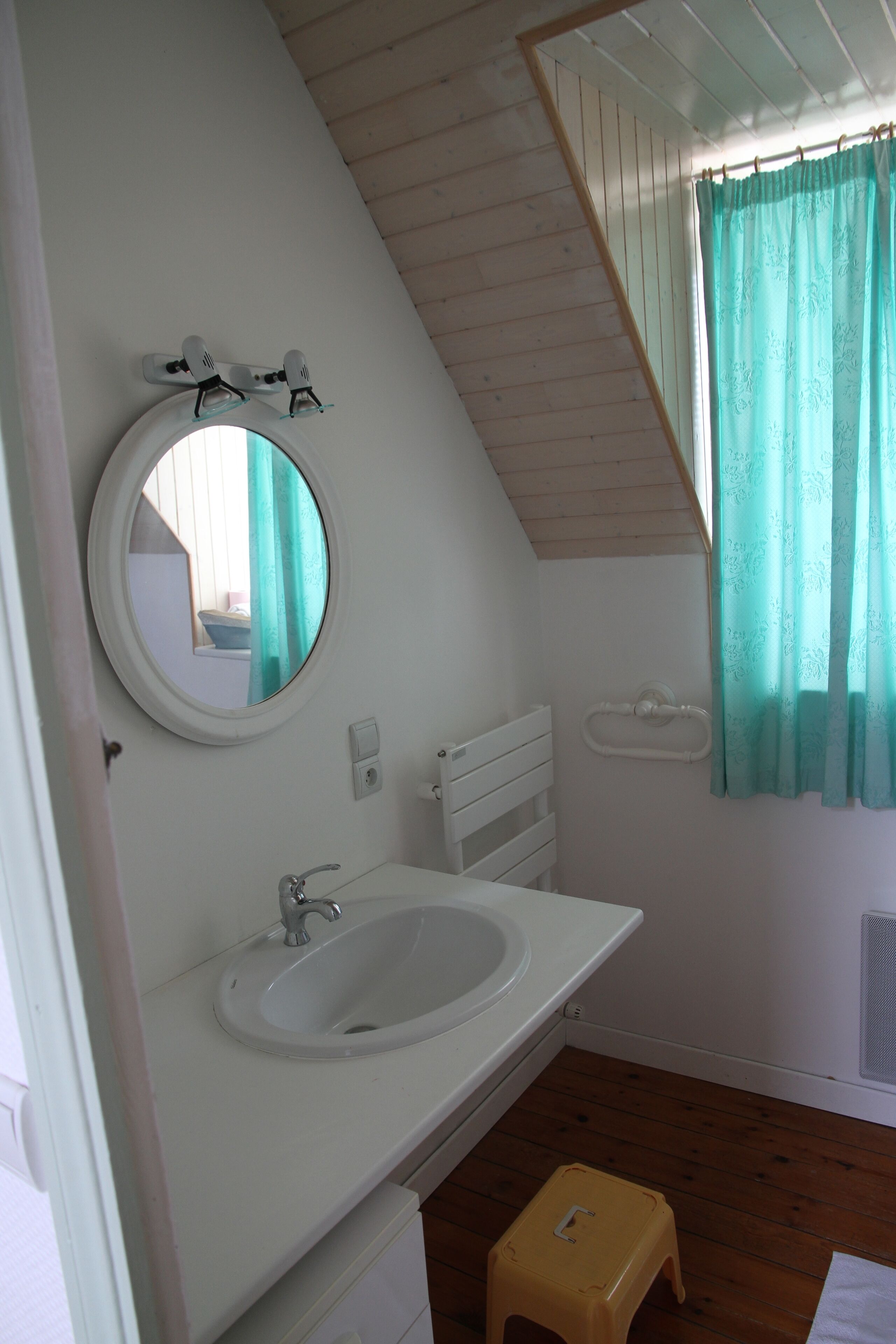 Un baño con un espejo redondo, un lavamanos y una ventana con cortinas.