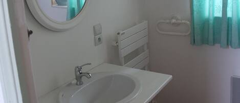 Un baño con un espejo redondo, un lavamanos y una ventana con cortinas.