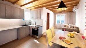 A modern kitchen with wooden beams, a dining area with a table set for a meal, and a living room with a sofa and a view of the outdoors.
