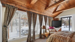 A bedroom with a large bed, wooden ceiling beams, and a TV on a stand.