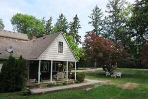 A house with a covered porch, a satellite dish, and a well-maintained lawn with trees and shrubs.