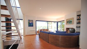 A spacious living area with a curved wooden bench, a staircase, and large windows offering a view of greenery. - VILLA SA CALETA:  6 beds, 5 baths  Front line Villa In Es Forti, Cala d´Or (Santanyí)