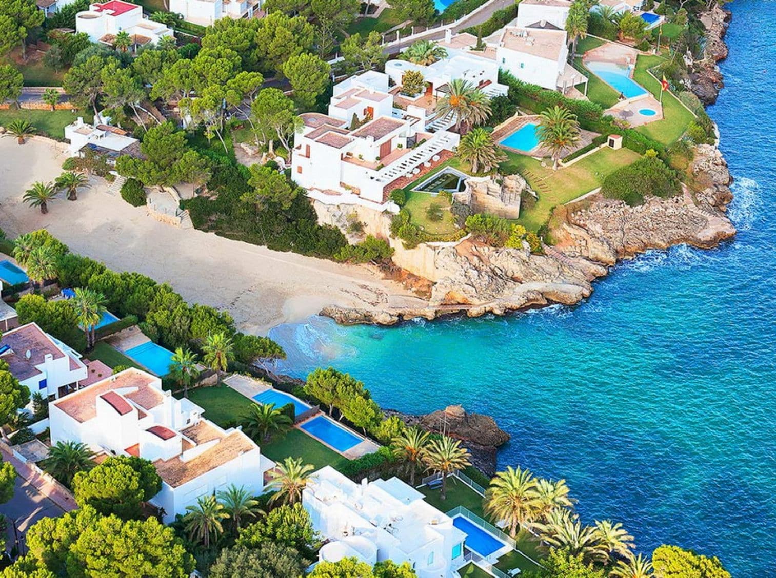 Vista aérea de una zona residencial costera con casas, una playa y un mar azul y despejado.