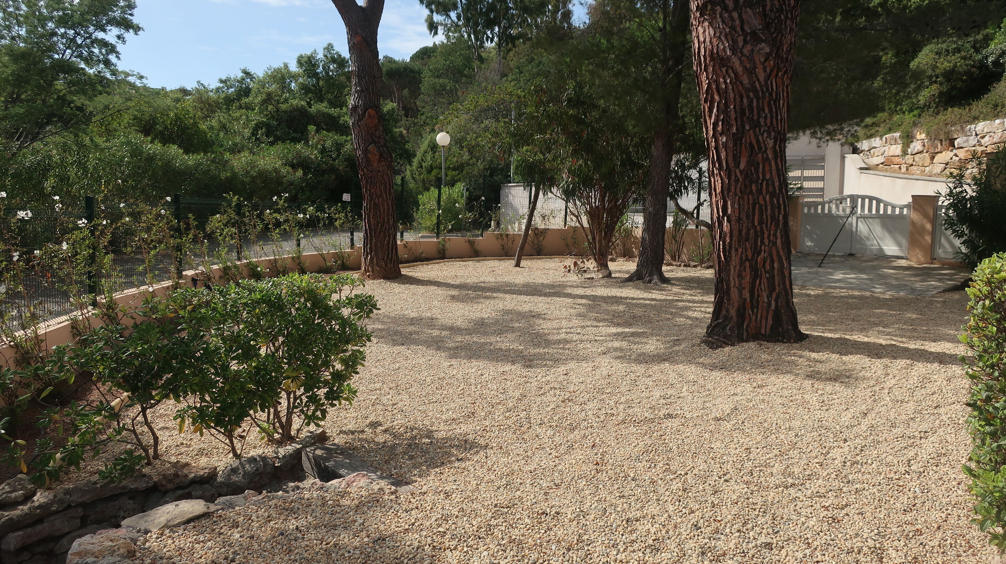 Un'area esterna curata con vialetti in ghiaia, alberi e un muro in pietra.