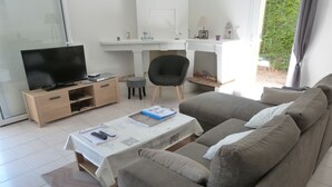 A living room with a sofa, a coffee table, a TV, and a small dining area. - House near La Cotinière -WIFI -heated pool -classified 4* Charente Tourisme (Saint-Pierre-d'Oléron)