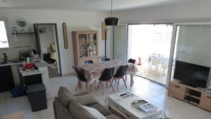A living room with a sofa, a coffee table, a dining table with chairs, a television, and a kitchen area with cabinets and a refrigerator. - House near La Cotinière -WIFI -heated pool -classified 4* Charente Tourisme (Saint-Pierre-d'Oléron)