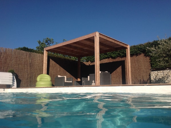 A wooden gazebo by a pool with a clear blue sky.