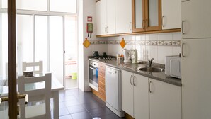 Una cocina con armarios blancos, estufa, fregadero y microondas. Se ve una ventana con vistas al exterior.