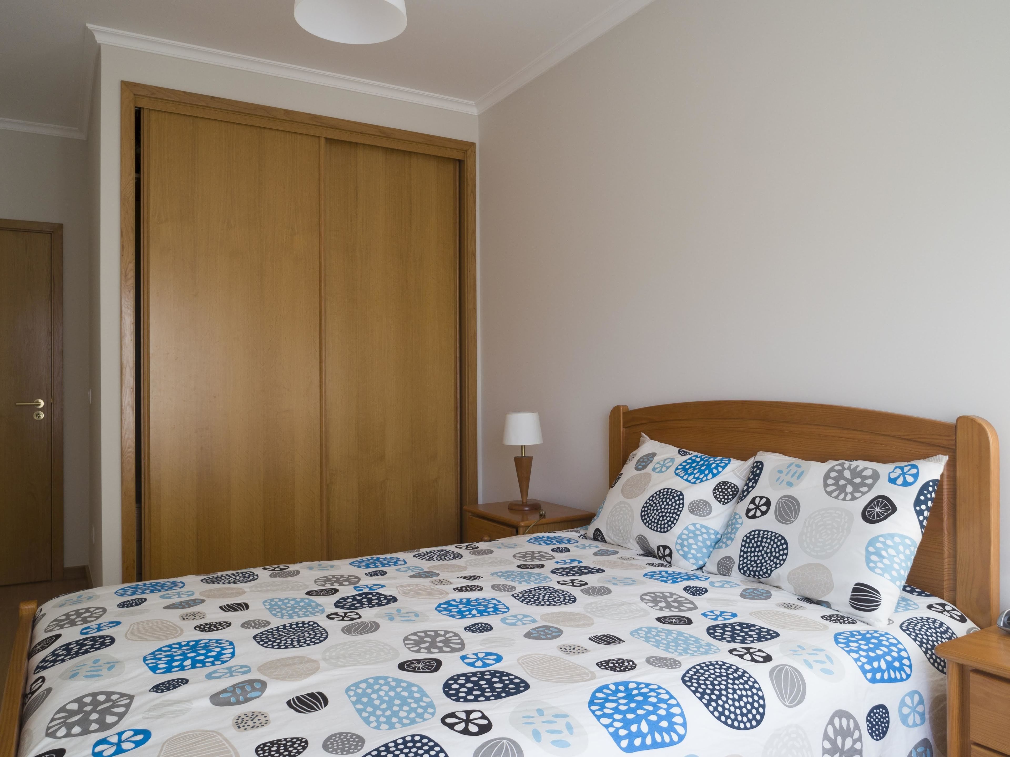 Un dormitorio con una cama de madera, una mesita de noche con una lámpara y un armario.