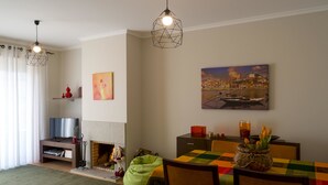 Una sala de estar acogedora con chimenea, una mesa de comedor con sillas, un sillón de felpa verde y dos lámparas colgantes.