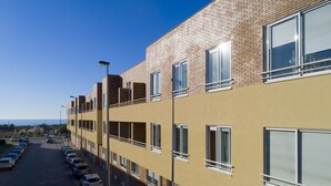 Un edificio de varios pisos con fachada de ladrillo y amplias ventanas. Hay un estacionamiento con varios autos estacionados al frente.