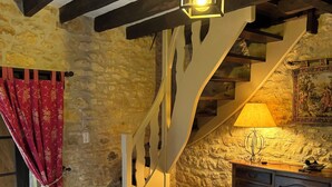 A rustic interior with a wooden staircase, stone walls, a wooden cabinet, and a patterned rug.