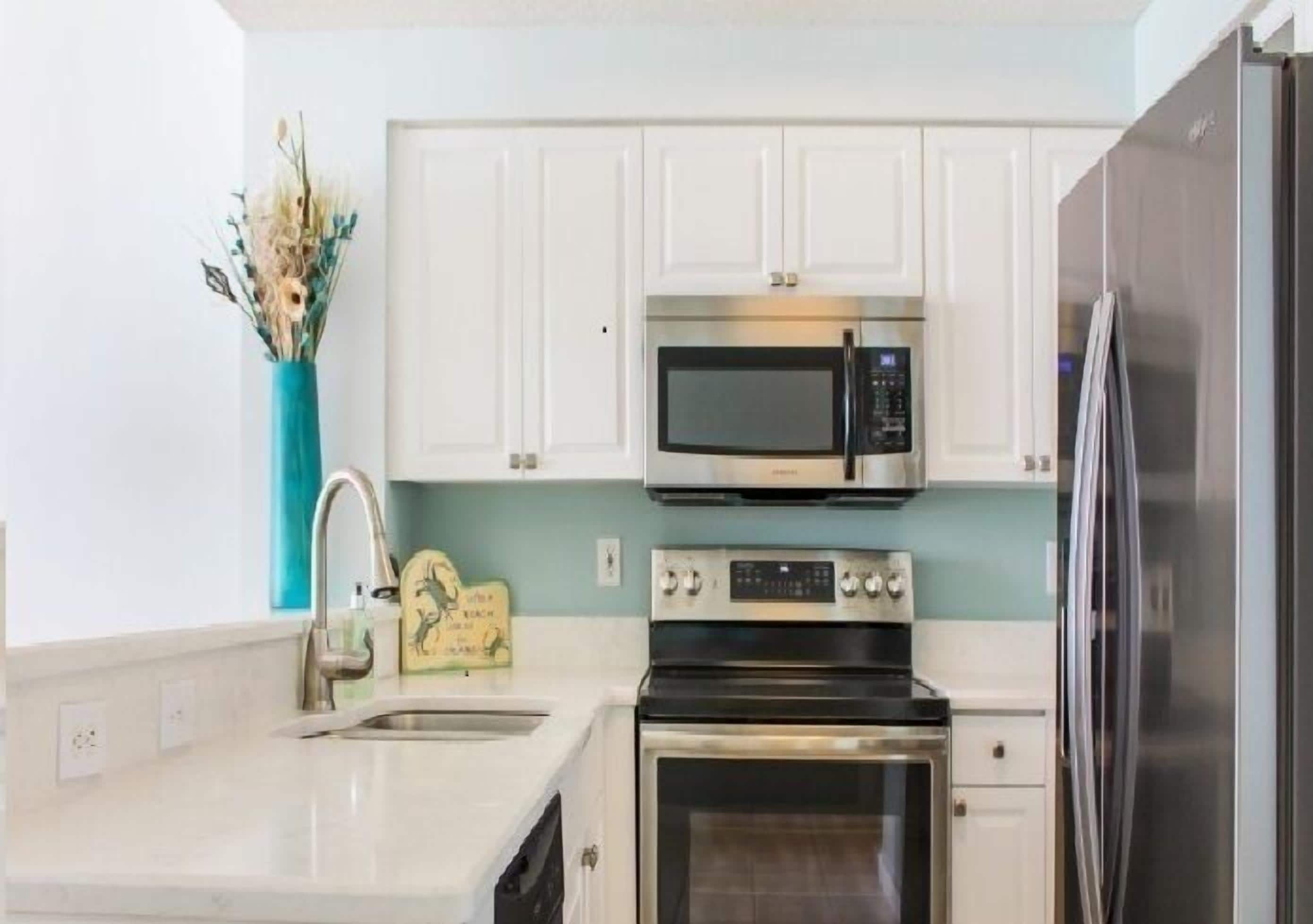 A modern kitchen with white cabinets, a stainless steel microwave, oven, and refrigerator.