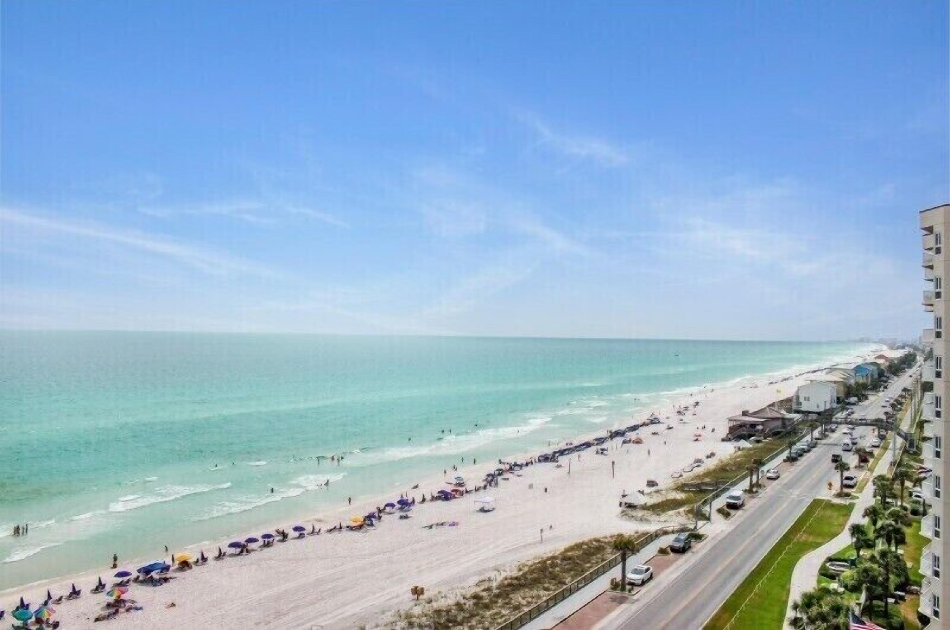 Una spiaggia con una strada che la costeggia, cielo sereno e edifici sullo sfondo.