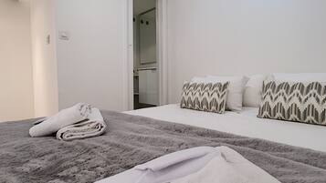 A hotel room with a bed, a folded towel, and a pair of slippers on the floor.