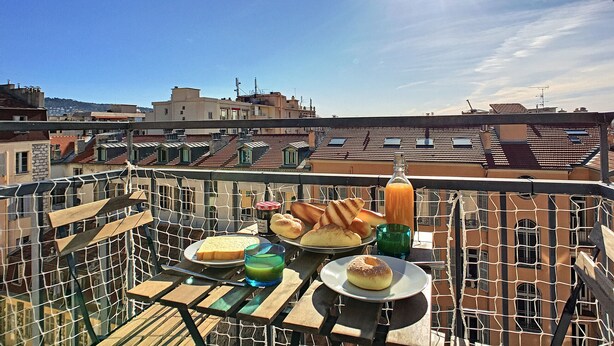En takterrass med ett bord dukat för frukost, med bröd, bakverk och ett glas juice.