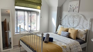 Een slaapkamer met een bed, een raam met zonwering, een radiator en een aan de muur hangend schilderij.