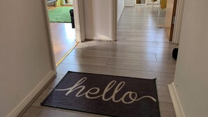 Een hal met een donkere deurmat waarop “hello” staat en een houten vloer.
