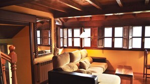 Een knus ingerichte kamer met een houten plafond, een bank, een klein tafeltje en een raam met veel ruitjes.