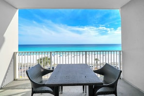A balcony with a view of the beach, a table, and two chairs.