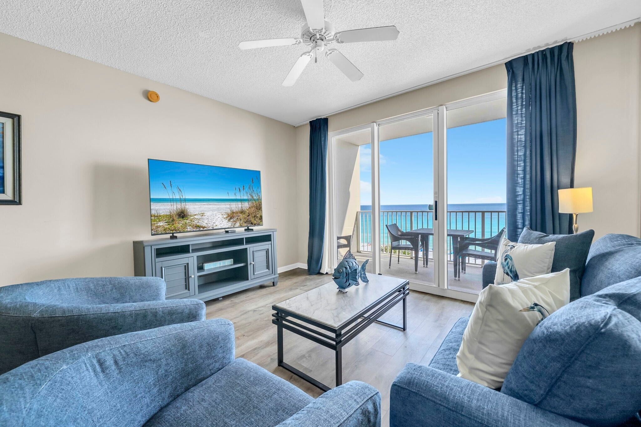 A living room with a TV, sofa, coffee table, and a view of the ocean through large sliding doors.