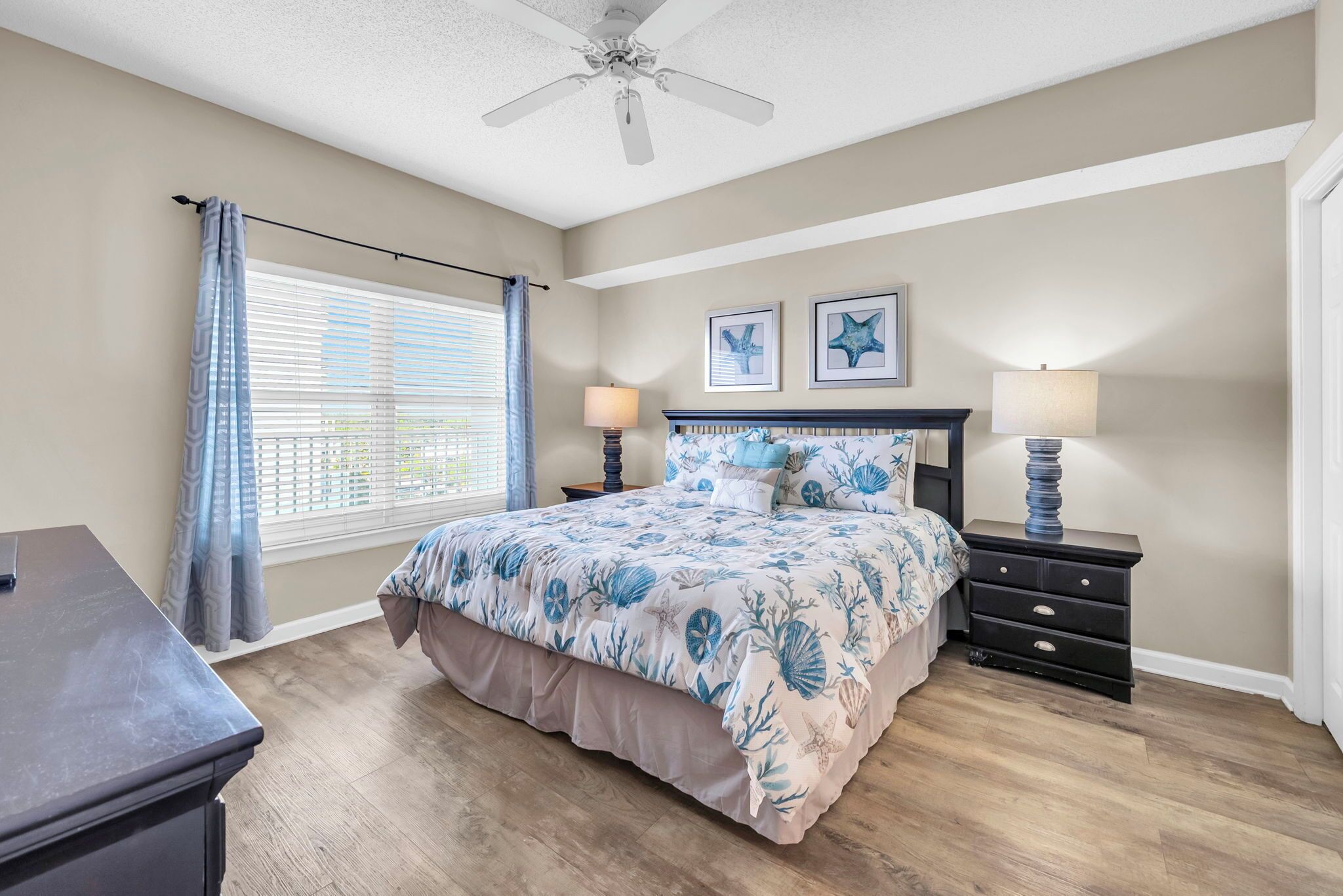 A bedroom with a bed, two bedside tables, a ceiling fan, and a window with blinds.