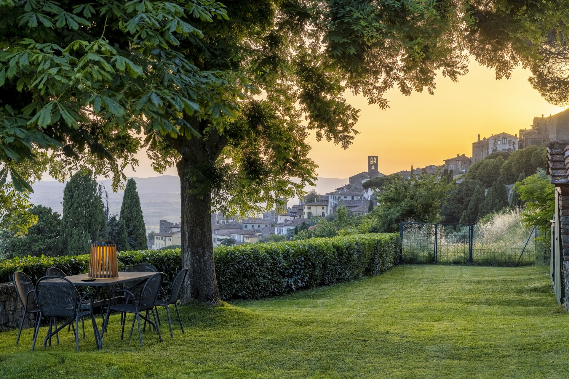 Ein Garten mit Tisch und Stühlen, einem Baum und Blick auf eine Stadt mit Gebäuden und einem Turm.