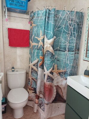 Une salle de bain équipée de toilettes, d’un lavabo et d’un rideau de douche à motifs marins.