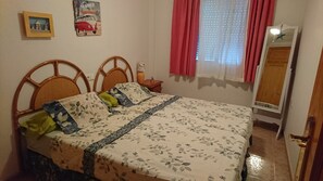 Une chambre à coucher avec un lit, une table de chevet, un miroir et un mur orné d’un tableau et d’une affiche.