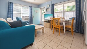 Una sala de estar con un sofá, una mesa de comedor con sillas, un televisor y una ventana con persianas.