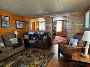 A cozy cabin interior with a wooden interior, a sofa, a chair, a rug, and a welcome sign.