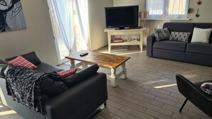 Un salón moderno con un sofá negro, una mesa de centro de madera, un sofá gris y un televisor de pantalla plana sobre un soporte blanco.