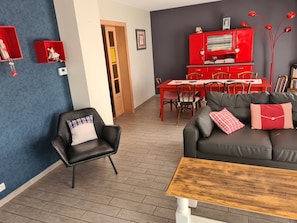 A living room with a black leather sofa, a wooden coffee table, and a dining area with a red table and chairs. - Lovely, comfortable detached house near Colmar and vineyards (Sundhoffen)