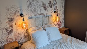 Un dormitorio con un mural floral, cabecera de madera, dos lámparas de noche y una cama con ropa blanca.