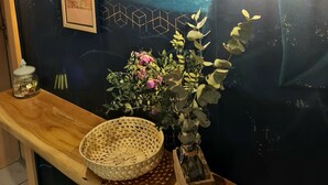 Una habitación de tonos oscuros con una encimera de madera, una bombilla, cuadros enmarcados y un florero con flores.
