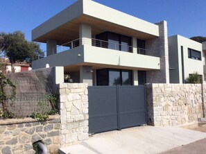 Uma casa moderna de dois andares com fachada de pedra, uma varanda e um portão cinza fechado.