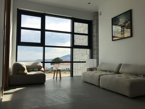 Uma sala de estar espaçosa, com uma janela grande, um sofá, uma poltrona e uma mesinha.