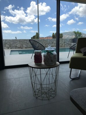 Quarto moderno com vista para uma piscina e uma parede de pedra. Há uma mesa redonda com dois potes de vidro em cima.