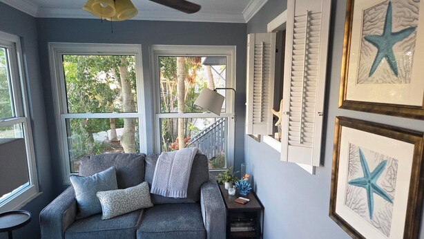 A cozy room with a grey sofa, a small table with decorative items, and a window with shutters. - Key West Style Townhome  Intercoastal Waterviews!!!
 (Indian Rocks Beach)