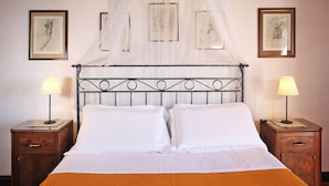 Een net opgemaakt bed met witte lakens, twee nachtkastjes met lampen, en kunstwerken aan de muur.